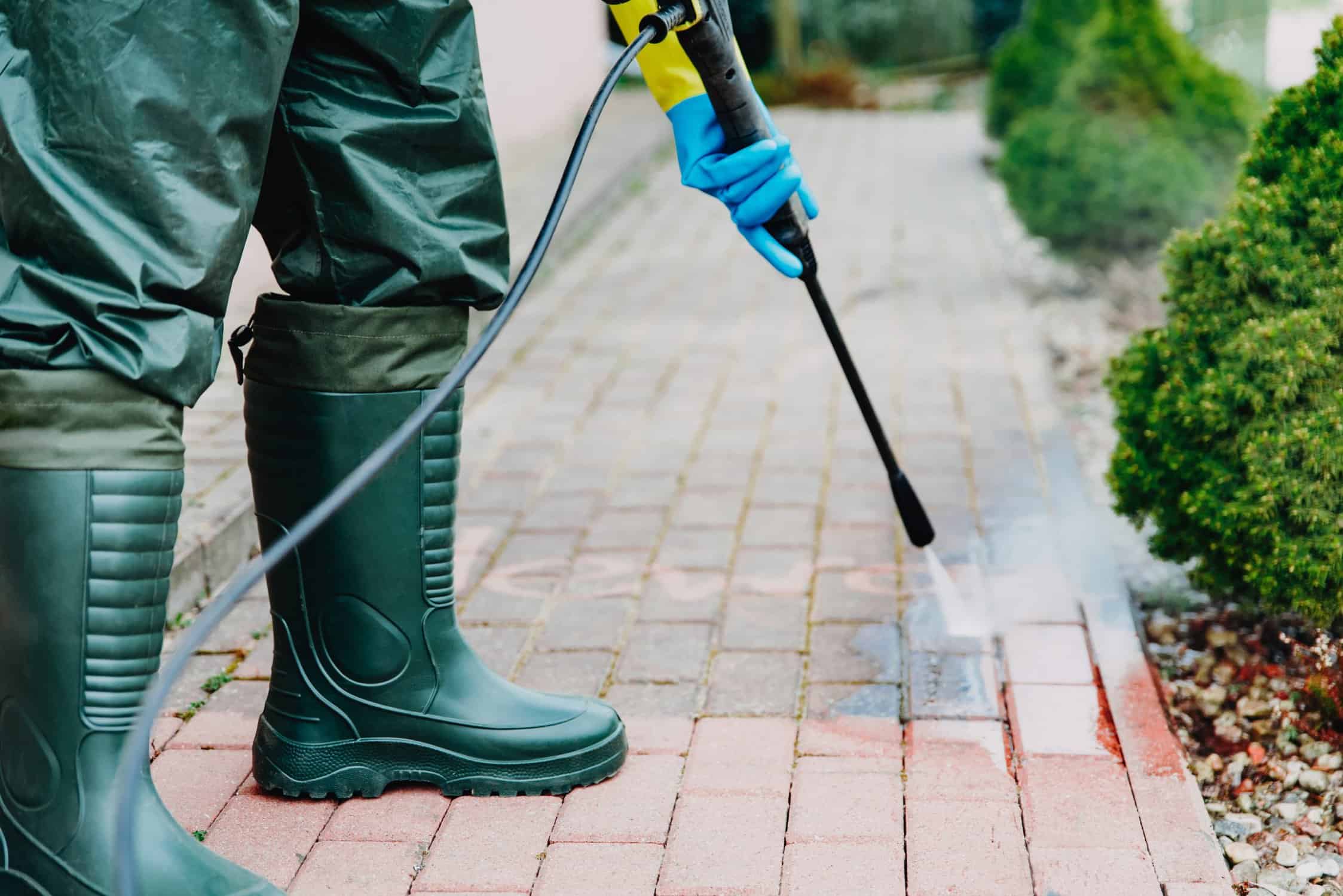 Man cleaning red, concrete pavement block using high pressure water cleaner.