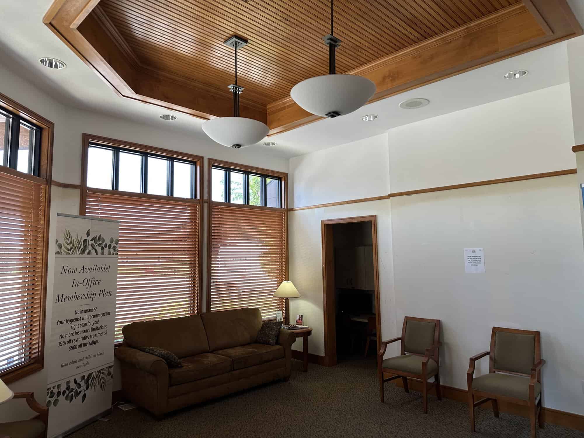 A cozy waiting room with a wooden ceiling, large windows, and comfortable seating.