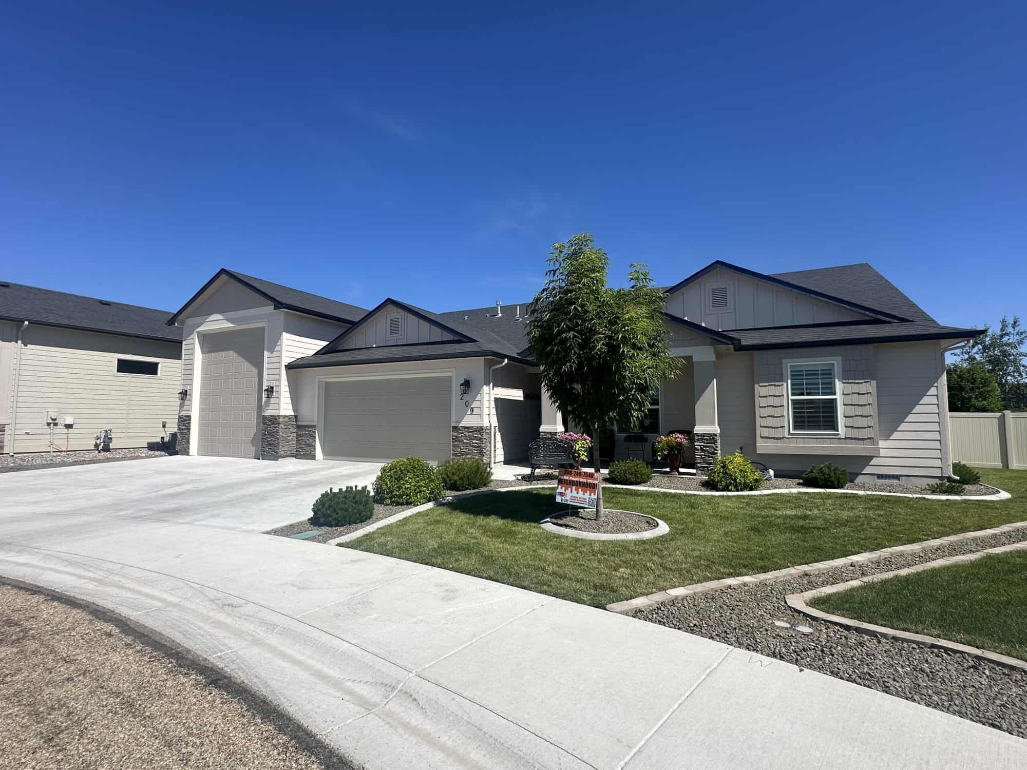 A modern, one-story house with a gray exterior and a black roof. The house features a two-car garage, a front porch, and a well-manicured lawn.