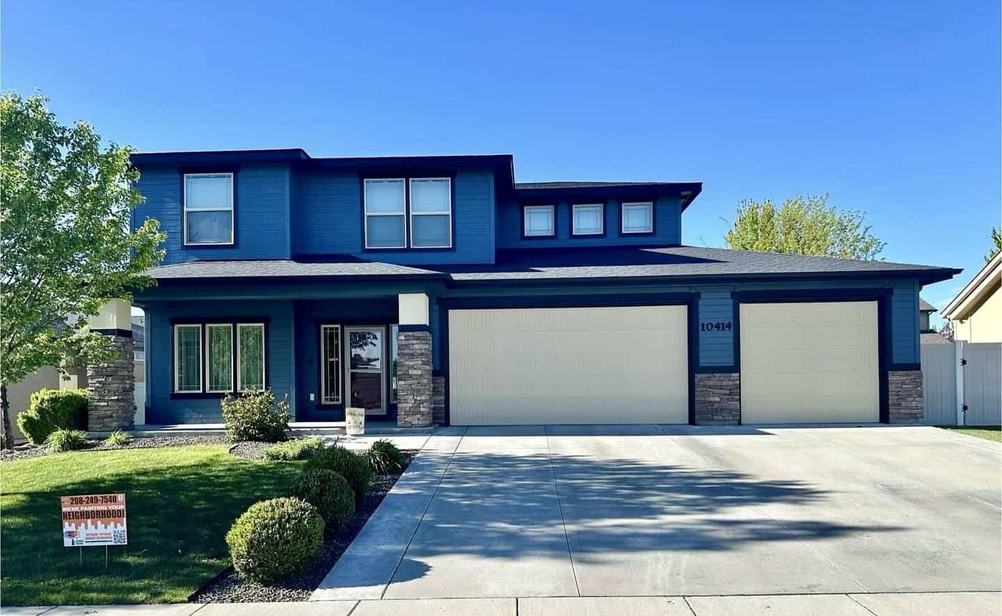 A two-story house with a striking blue exterior and a stone accent wall. The house features a two-car garage, a front porch, and a well-manicured lawn.