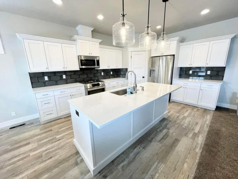 Freshly painted white kitchen cabinets with a large island, black subway tile backsplash, and pendant lighting, cabinet painting by Lagunas Painting in Boise, Idaho