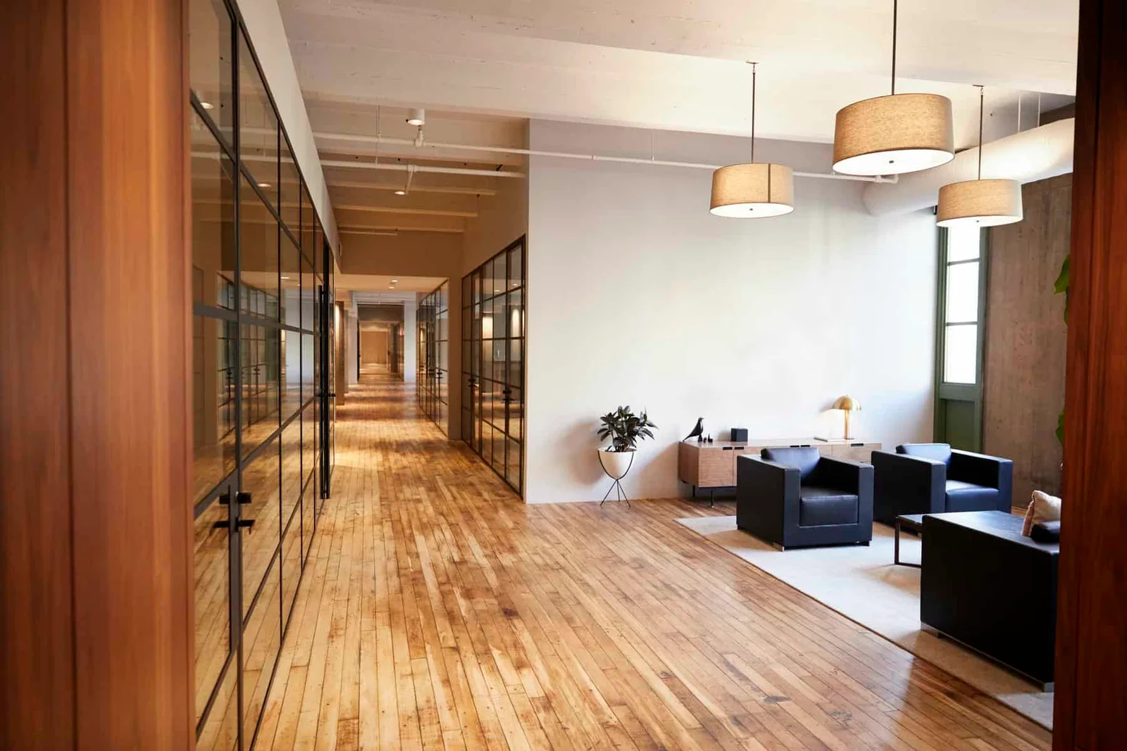 Modern office hallway with glass-panel partitions, wood flooring, and warm pendant lighting, interior commercial painting by Lagunas Painting in the Treasure Valley, Idaho