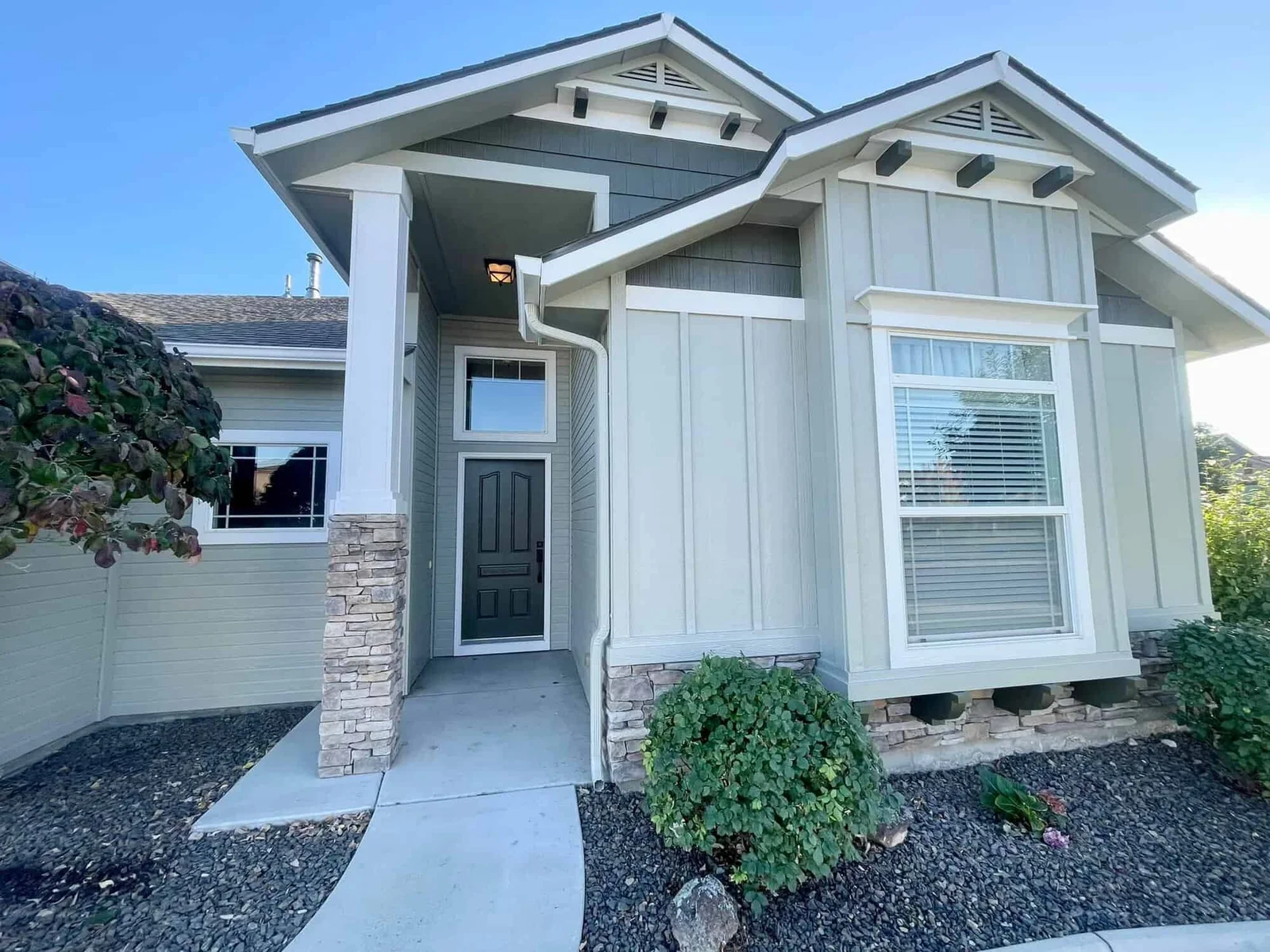 Freshly painted light gray exterior of a single-family home with board-and-batten siding and stone accents, exterior house painting by Lagunas Painting in Nampa, Idaho
