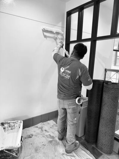 Lagunas Painting professional rolling paint on an interior wall near a black-framed window in Caldwell, Idaho