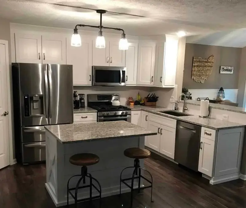 Modern kitchen with freshly painted white cabinets, stainless appliances, and a granite island, cabinet painting and refinishing by Lagunas Painting in Caldwell, Idaho