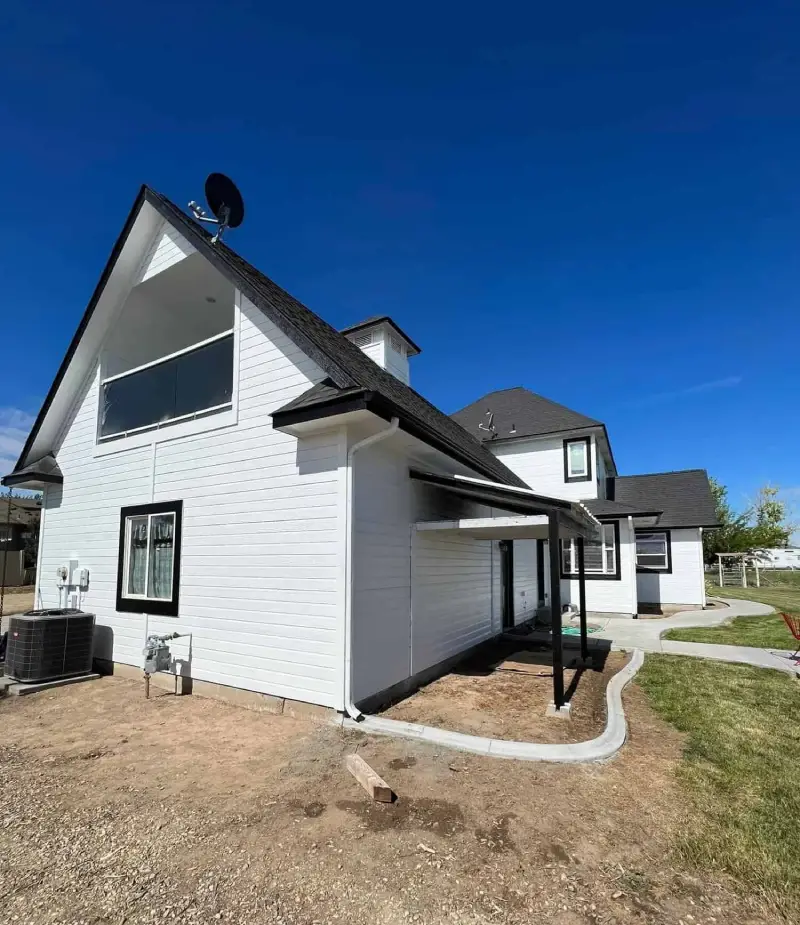 Two-story white house with a dark shingle roof and a freshly painted exterior against a clear blue sky, by Lagunas Painting in the Treasure Valley, Idaho